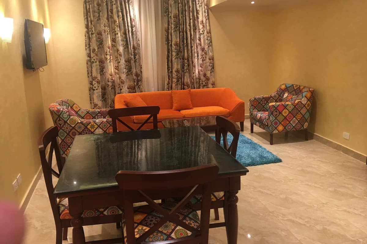 Ein Essbereich mit einem Glastisch, Holzstühlen, einem orangefarbenen Sofa und gemusterten Sesseln.