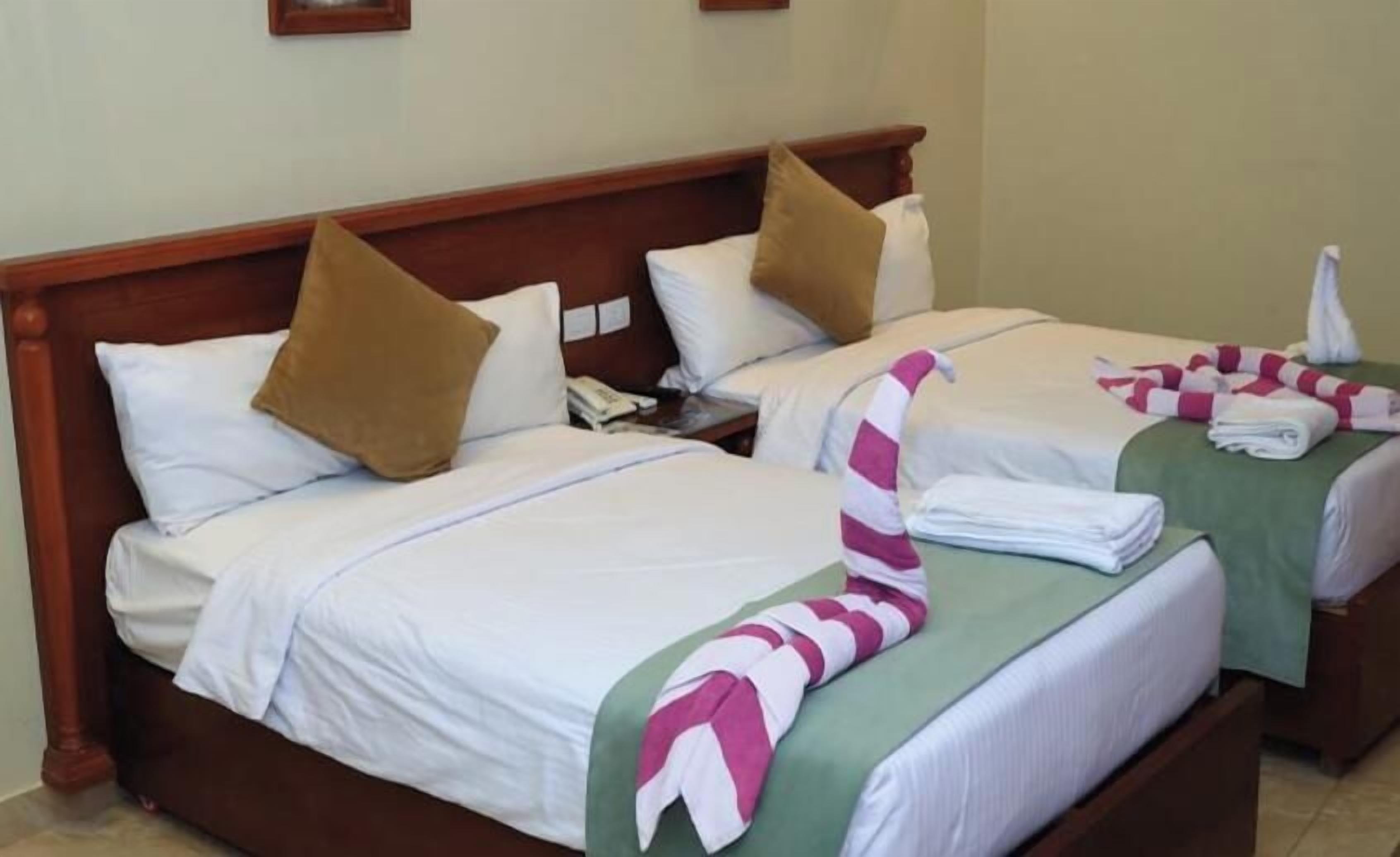 A hotel room with two beds, each with a pillow, a bedside table, and a striped towel.