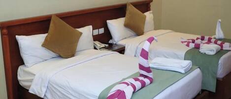 A hotel room with two beds, each with a pillow, a bedside table, and a striped towel.