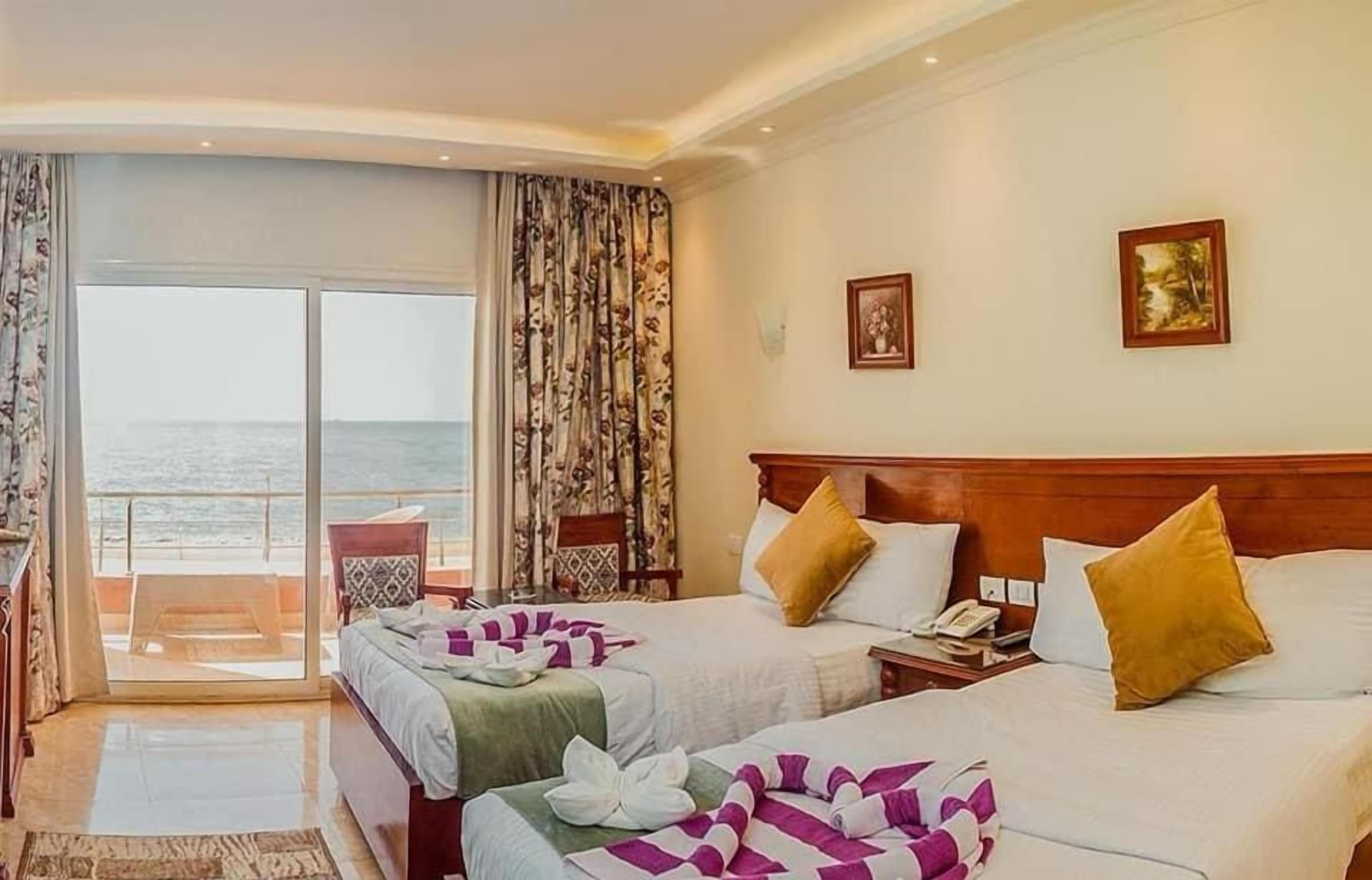 Quarto de hotel com duas camas, vista para o mar e varanda.