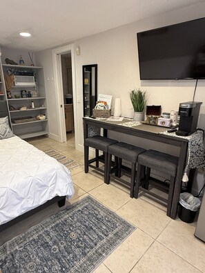 A modern bedroom with a bed, a desk, a chair, a television, and a coffee machine.