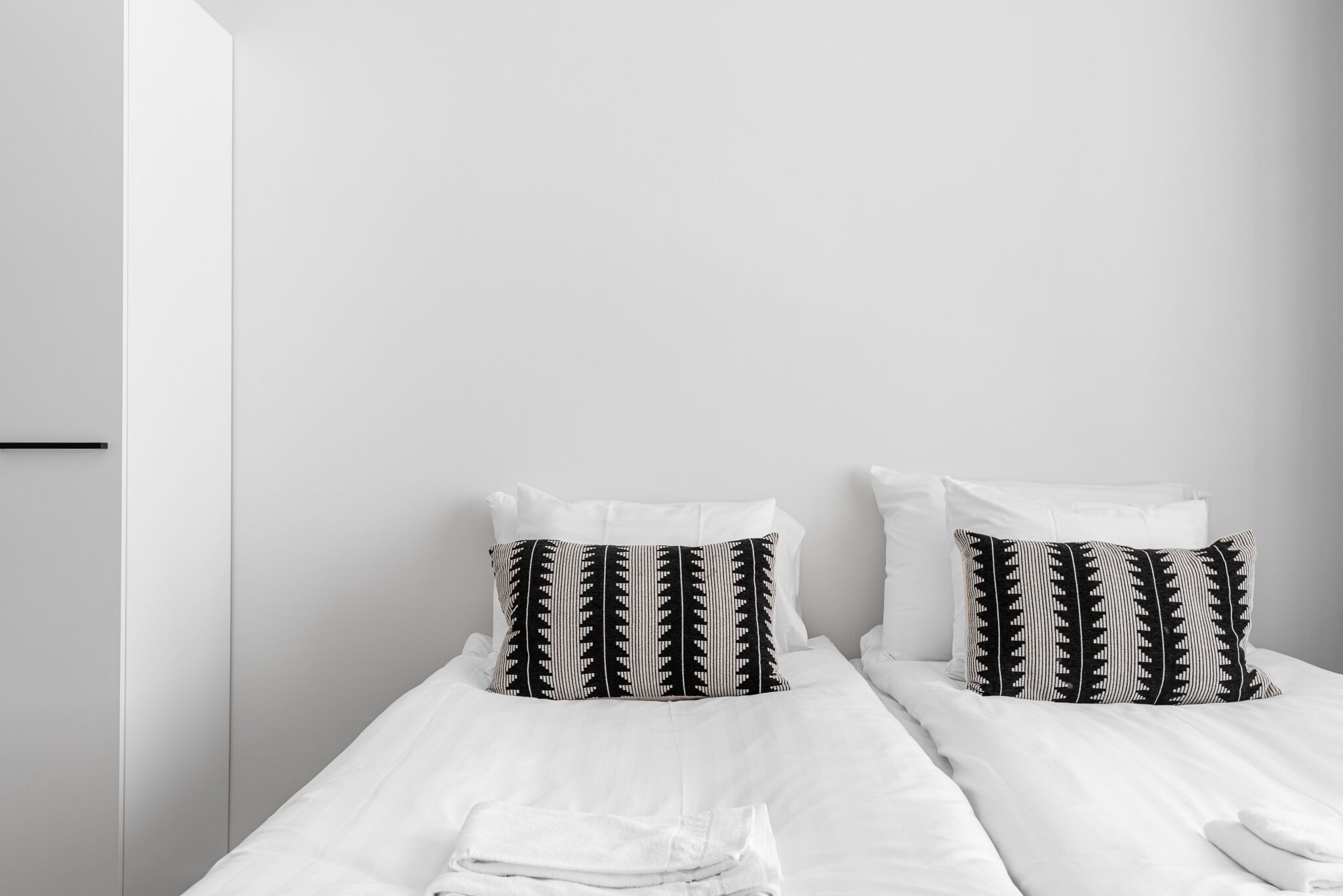 Una cama bien hecha con ropa blanca y dos almohadas estampadas en blanco y negro.