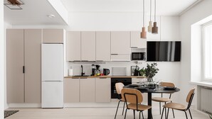A modern kitchen with a dining area, featuring a refrigerator, microwave, and a dining table with chairs. - Prime Apartments Pori Central (Pori)