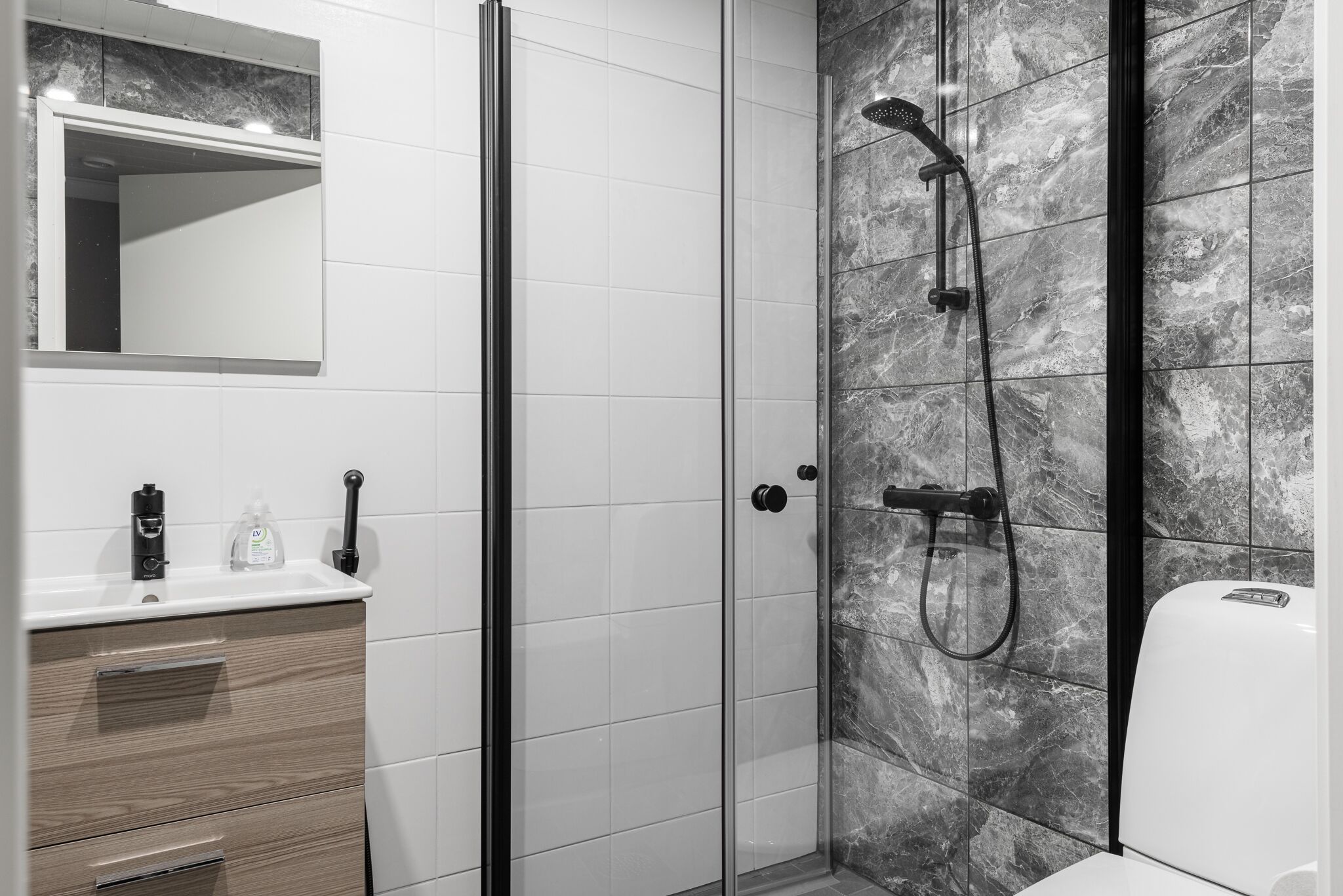 A modern bathroom with a glass shower enclosure, a white sink with a mirror above it, and a marble-tiled wall.