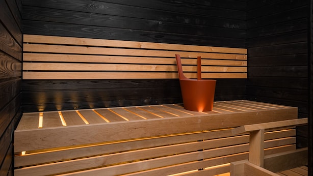 A wooden bench with a copper bucket in a room with dark wooden walls. - Prime Apartments Pori Central (Pori)