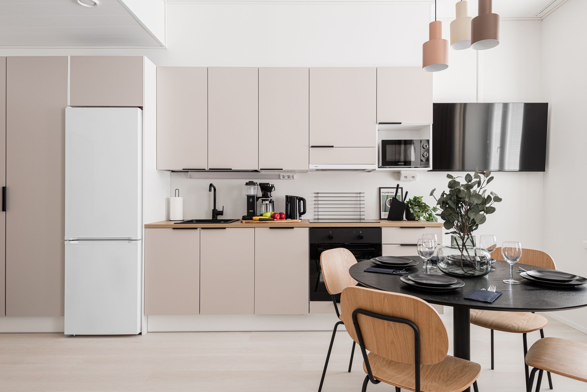 A modern kitchen with a refrigerator, microwave, and stove. There is a dining table with chairs and a vase of flowers.