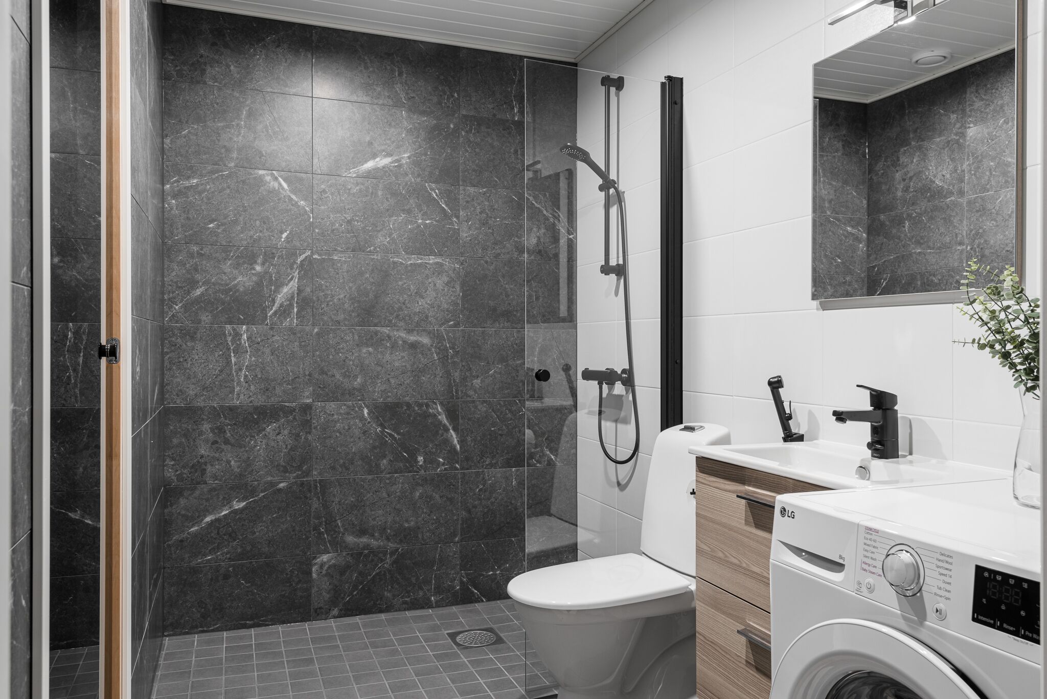 A modern bathroom with a walk-in shower, a toilet, and a washing machine.
