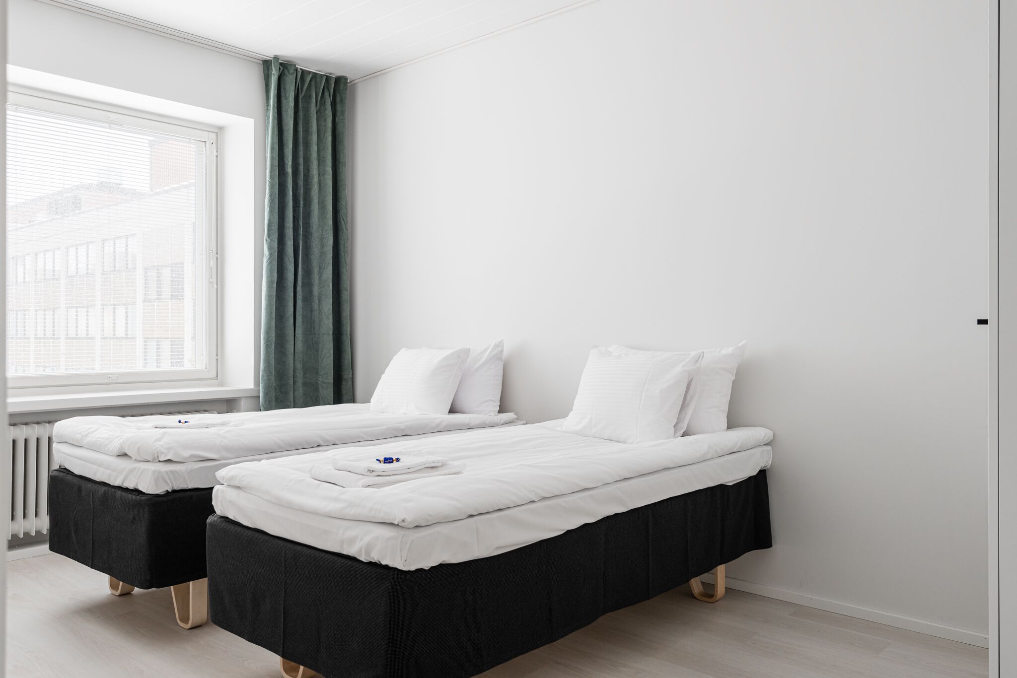 A hotel room with two single beds, a window with a view of buildings, and a radiator.