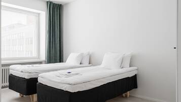 A hotel room with two single beds, a window with a view of buildings, and a radiator.