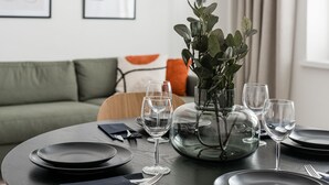 A dining table set with plates, glasses, and cutlery, a vase with greenery, and a modern sofa in the background. - Prime Apartments Pori Central (Pori)