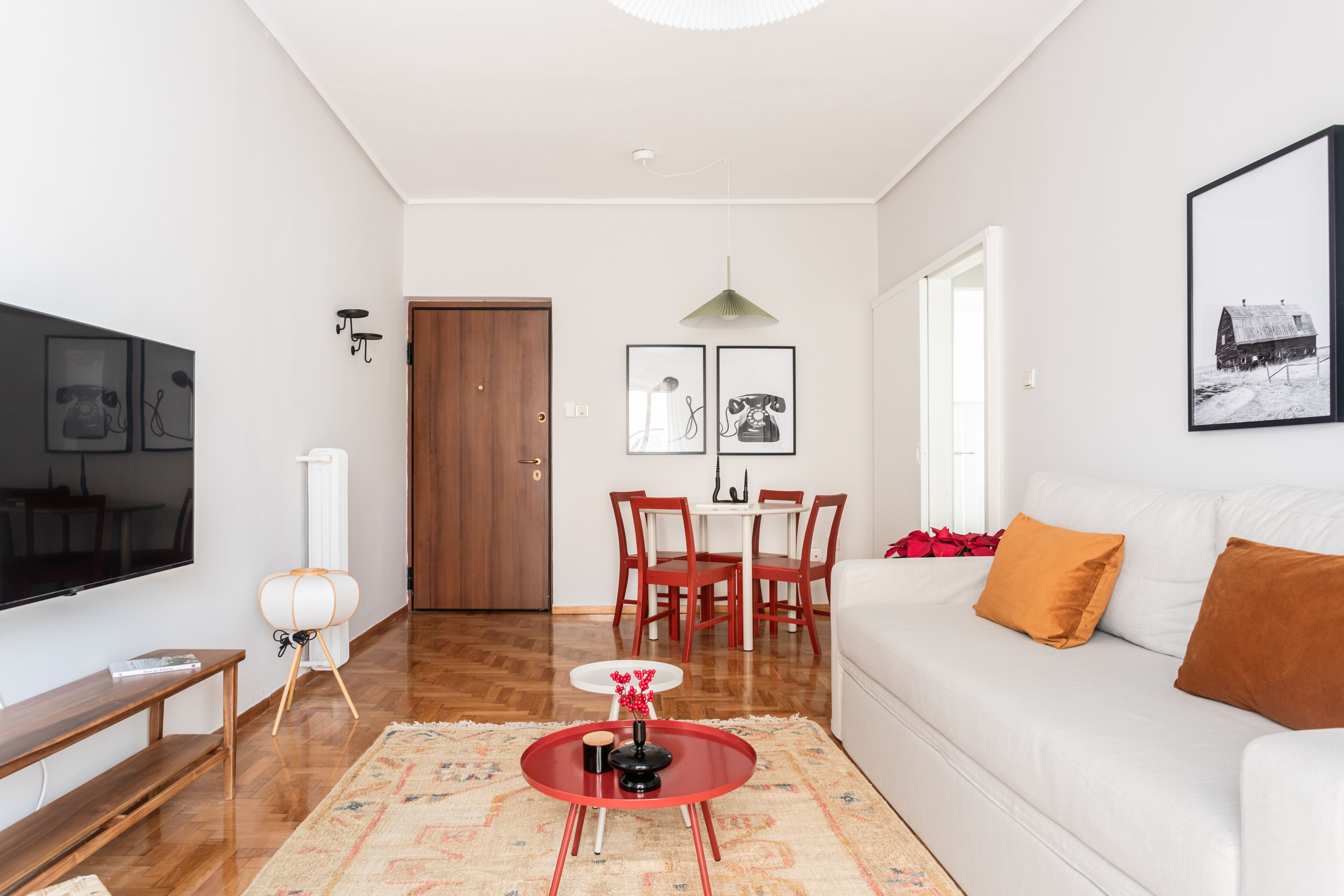 Ein modernes Wohnzimmer mit einem weißen Sofa, einem rot-weißen Couchtisch, Holzboden und einem Essbereich mit weißem Tisch und roten Stühlen.