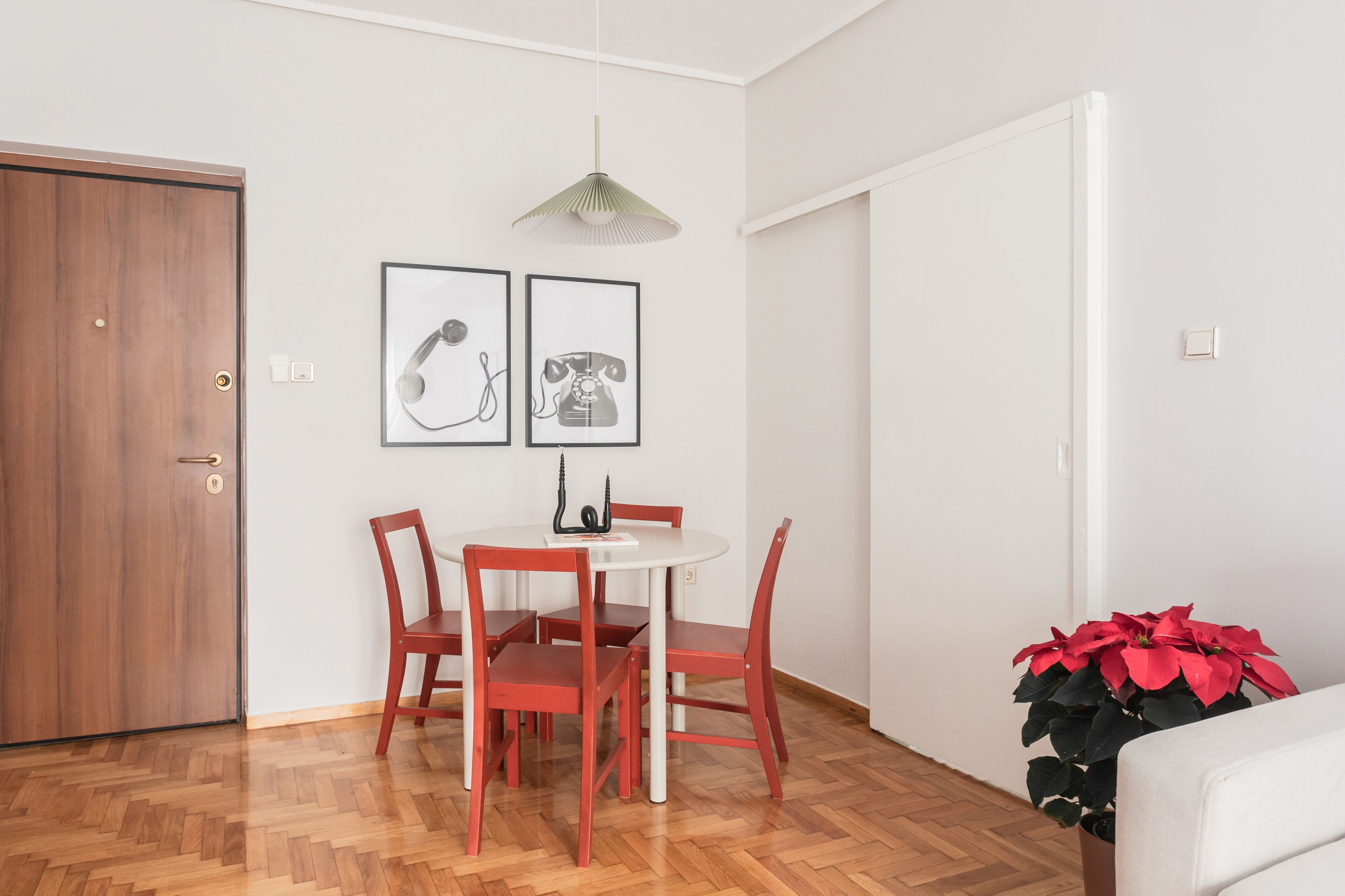 A dining area with a wooden herringbone floor, a white table, red chairs, and two framed pictures on the wall.