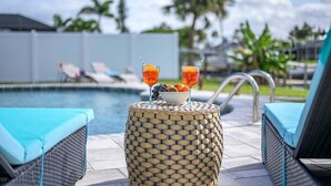 A poolside area with lounge chairs, a round table with a fruit bowl and drinks, and a clear view of the pool.