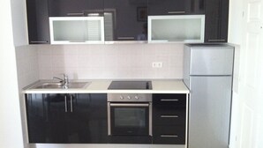 A compact kitchen with black cabinets, a microwave, a stove, and a refrigerator. - Two-bedroom apartment with a terrace (Novalja)