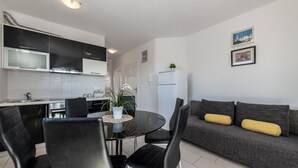 A modern kitchen with black cabinets, a white refrigerator, and a dining area with a glass table and black chairs. - Two-bedroom apartment with a terrace (Novalja)