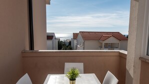 A balcony with a table and chairs, a potted plant, and a view of buildings and a body of water. - Two-bedroom apartment with a terrace (Novalja)