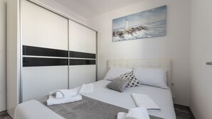 A hotel room with a bed, a painting of a lighthouse, a wardrobe, and a neatly made bed with towels. - Two-bedroom apartment with a terrace (Novalja)