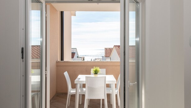 A balcony with a table and chairs, a small potted plant, and a view of the sea. - Two-bedroom apartment with a terrace (Novalja)
