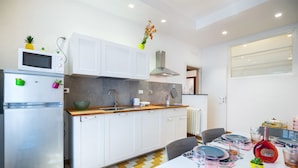 A modern kitchen with white cabinets, a microwave, and a refrigerator. There is a dining table set with plates, glasses, and a red bottle. - Apartment via Milizia 3br/3bt (Roma)