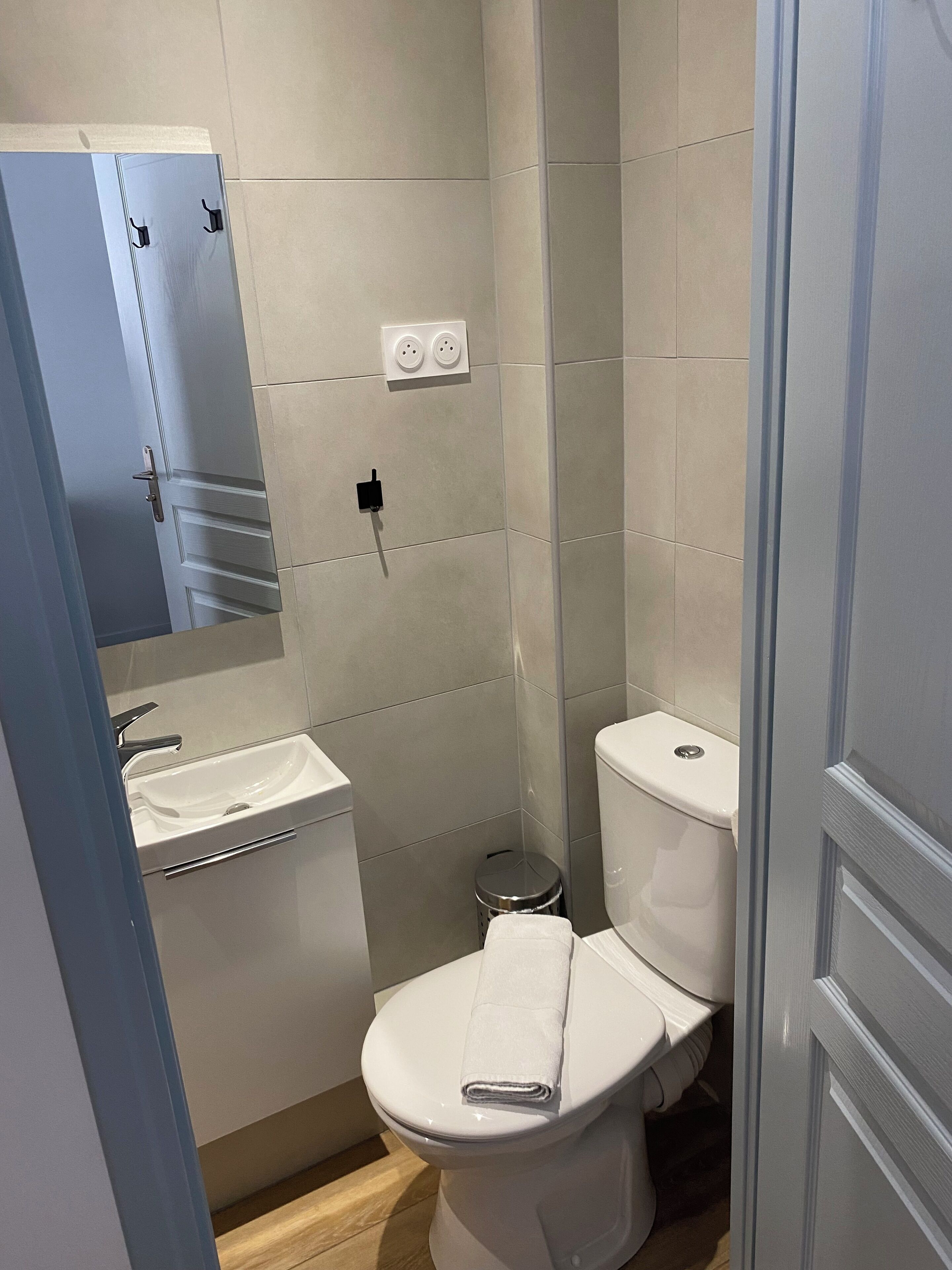 A bathroom with a white toilet, a sink, and a mirror. There are two electrical outlets on the wall.