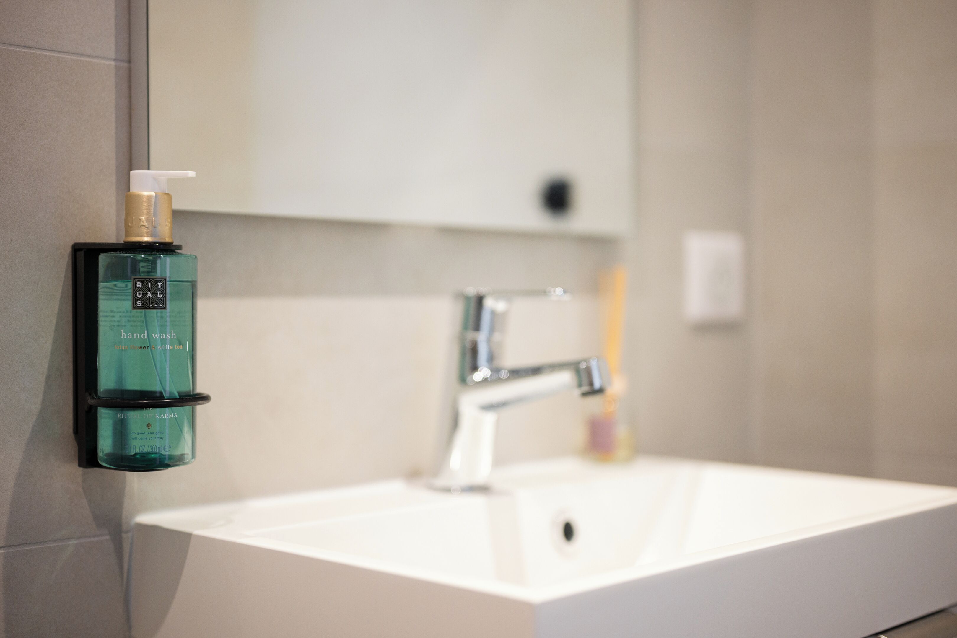 A bathroom with a white sink, a mirror, and a hand wash dispenser.