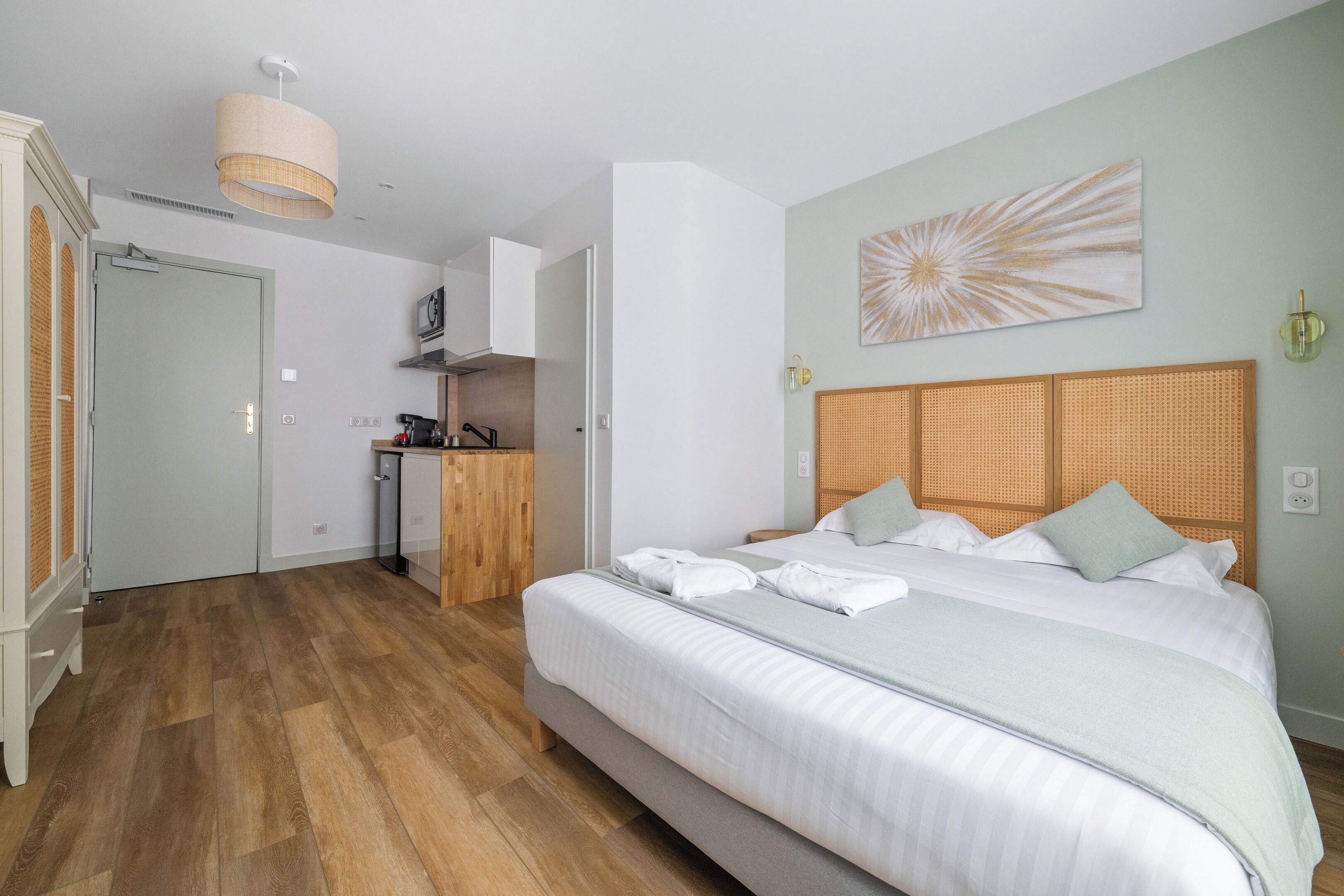 A bedroom with a large bed, a wooden floor, a kitchenette, and a bathroom.