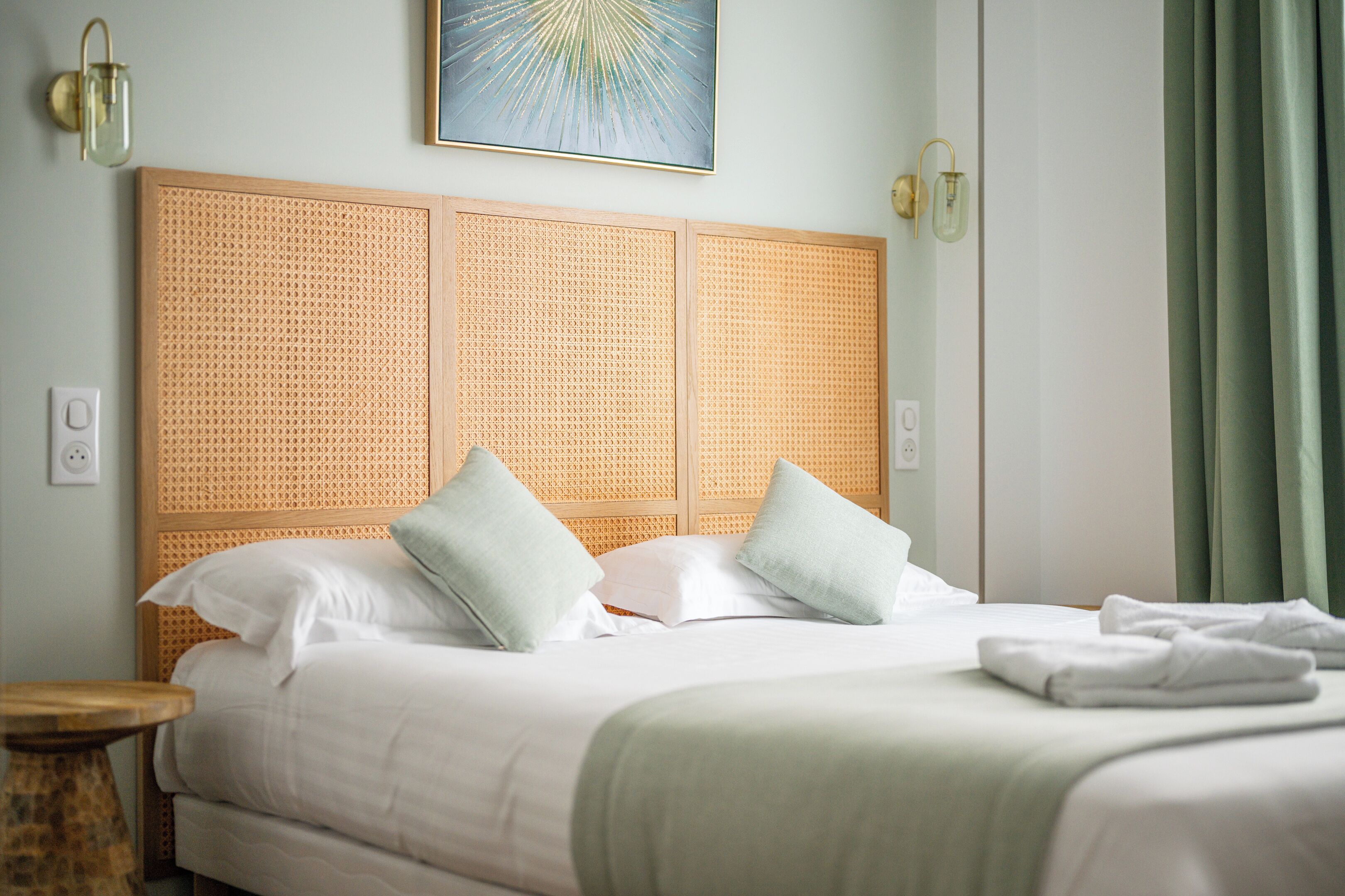 A neatly made bed with white linens and two pillows, a wooden headboard, and a green curtain.