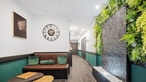 A hallway with a bench, a clock, and a wall with greenery. - L'App-Art (Nice)