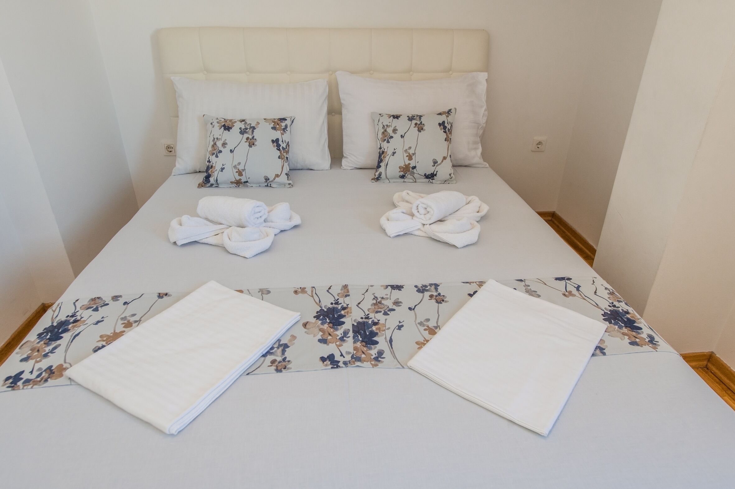 Ein ordentlich bezogenes Bett mit blumigen Kissen und einer passenden Tagesdecke.