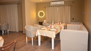 A dining area with a long table set for four, surrounded by cushioned chairs, a sofa, and a small round table with a mirror.
