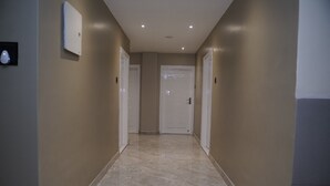 A hallway with beige walls and a marble floor, leading to a door at the end.
