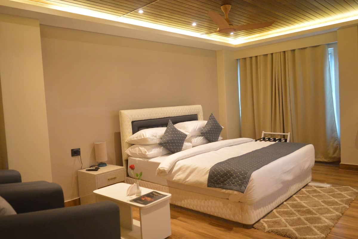 Een moderne hotelkamer met een groot bed, nachtkastjes en een uitzicht buiten door een raam met gordijnen.