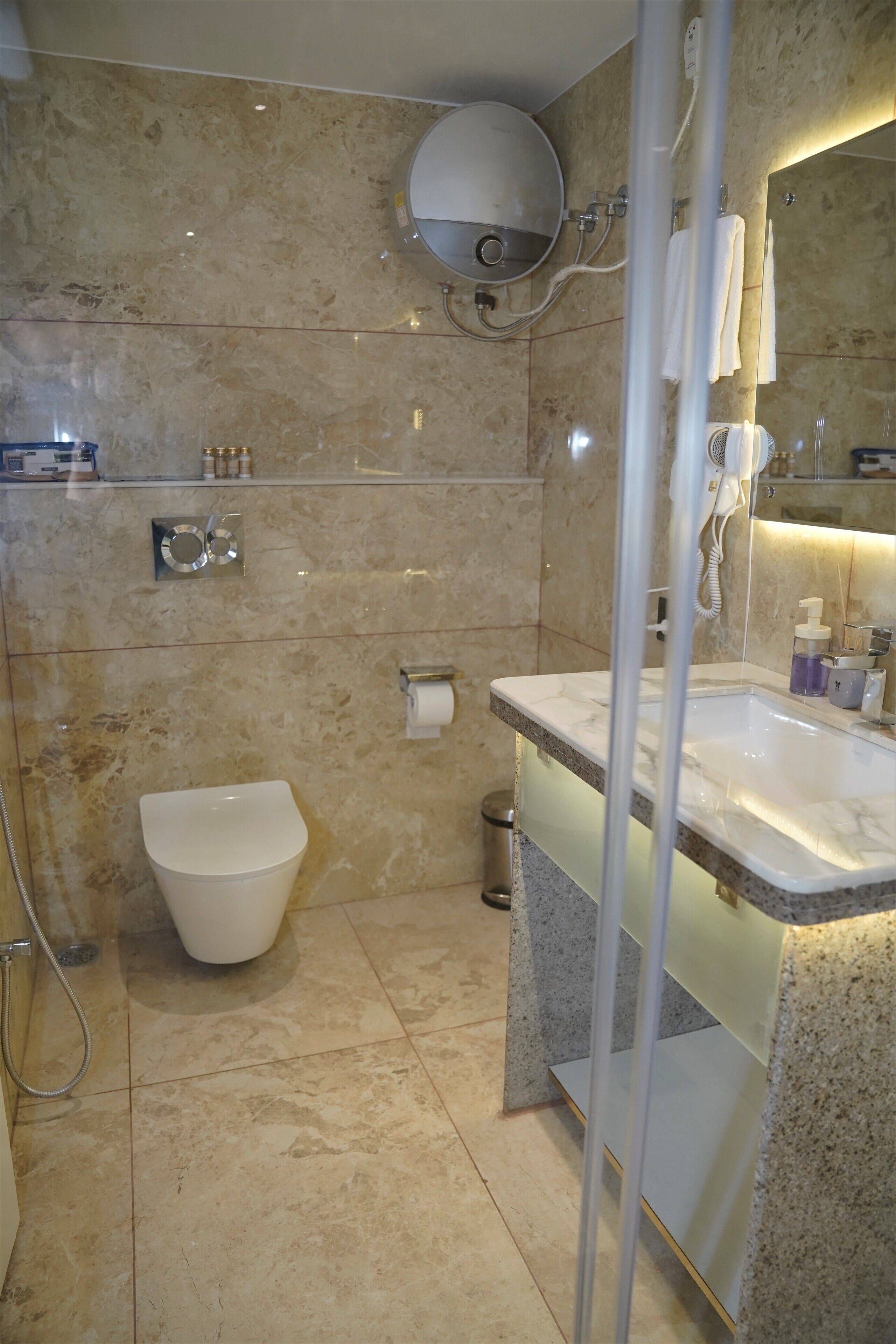 A modern bathroom with a marble floor, a toilet, a sink with a mirror, and a shower area.