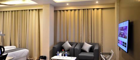 A modern hotel room with a bed, a sofa, a coffee table, and a TV mounted on the wall.