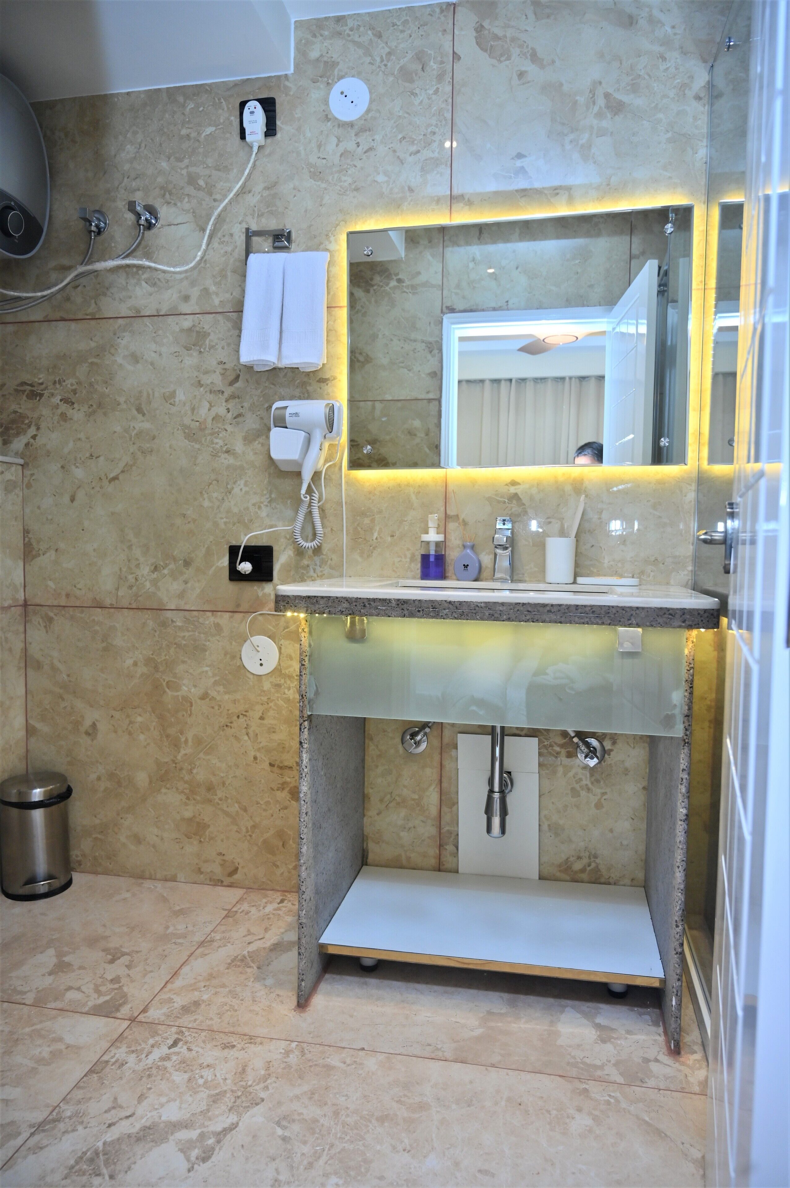 Un baño con piso de mármol, lavamanos de vidrio con espejo, secador de pelo y toallero.