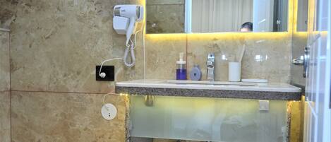 Uma casa de banho com chão de mármore, lavatório de vidro com espelho, secador de cabelo e porta-toalhas.