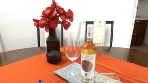 A dining table with a bottle of wine, a glass, a decorative vase with red flowers, a small woven basket, and a wrapped gift. - Casa Mim in Cabras (Cabras)