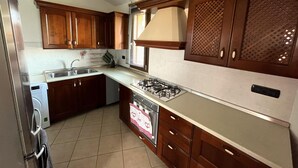 A kitchen with wooden cabinets, a stainless steel sink, a dishwasher, and a gas stove. - Casa Mim in Cabras (Cabras)