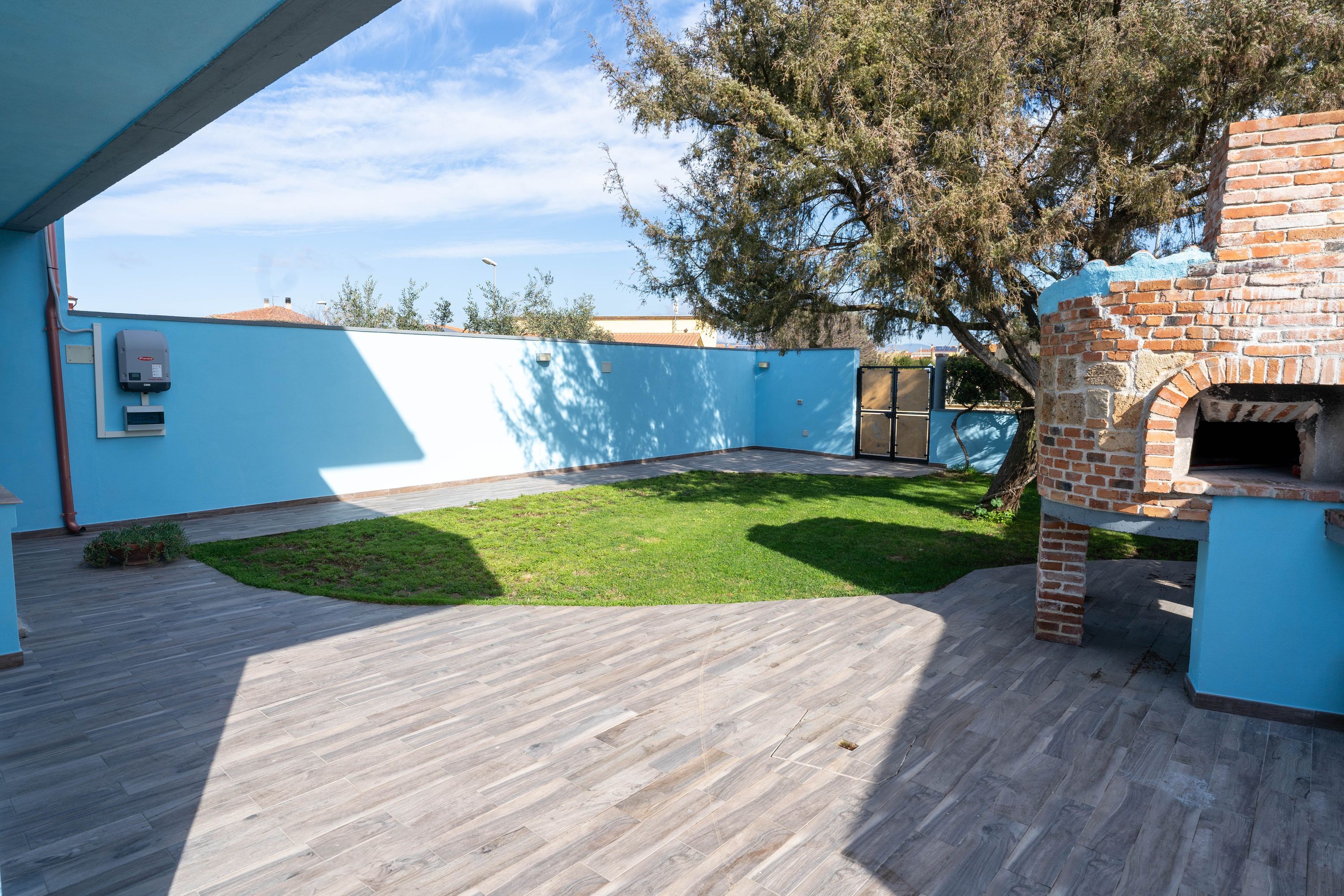 An outdoor patio with a brick oven, a blue wall, and a grassy area.