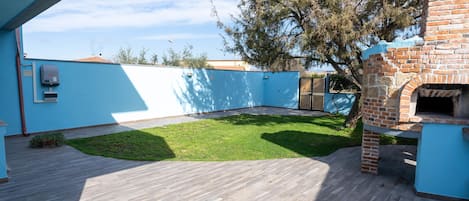 An outdoor patio with a brick oven, a blue wall, and a grassy area.