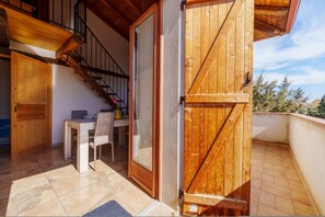 Ein hölzerner Balkon mit einer Schiebetür, ein Essbereich mit Tisch und Stühlen und eine Treppe zu einer oberen Ebene.