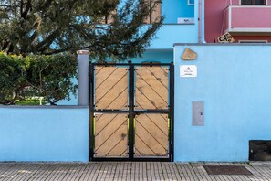 Un mur bleu avec un portail en métal, une enseigne indiquant « CASA », et un arbre en arrière-plan.
