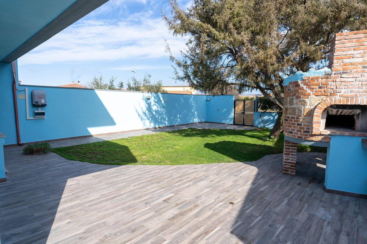 Eine Terrasse im Freien mit einem Backofen aus Ziegeln, einer blauen Wand und einer Rasenfläche.