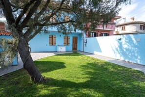 Il s’agit d’une maison d’habitation à l’extérieur bleu, avec un petit jardin devant et un arbre.