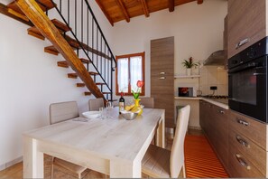 Une cuisine moderne dotée d’un four encastré, un coin repas avec une table et des chaises en bois, et un escalier avec des rampes en bois.