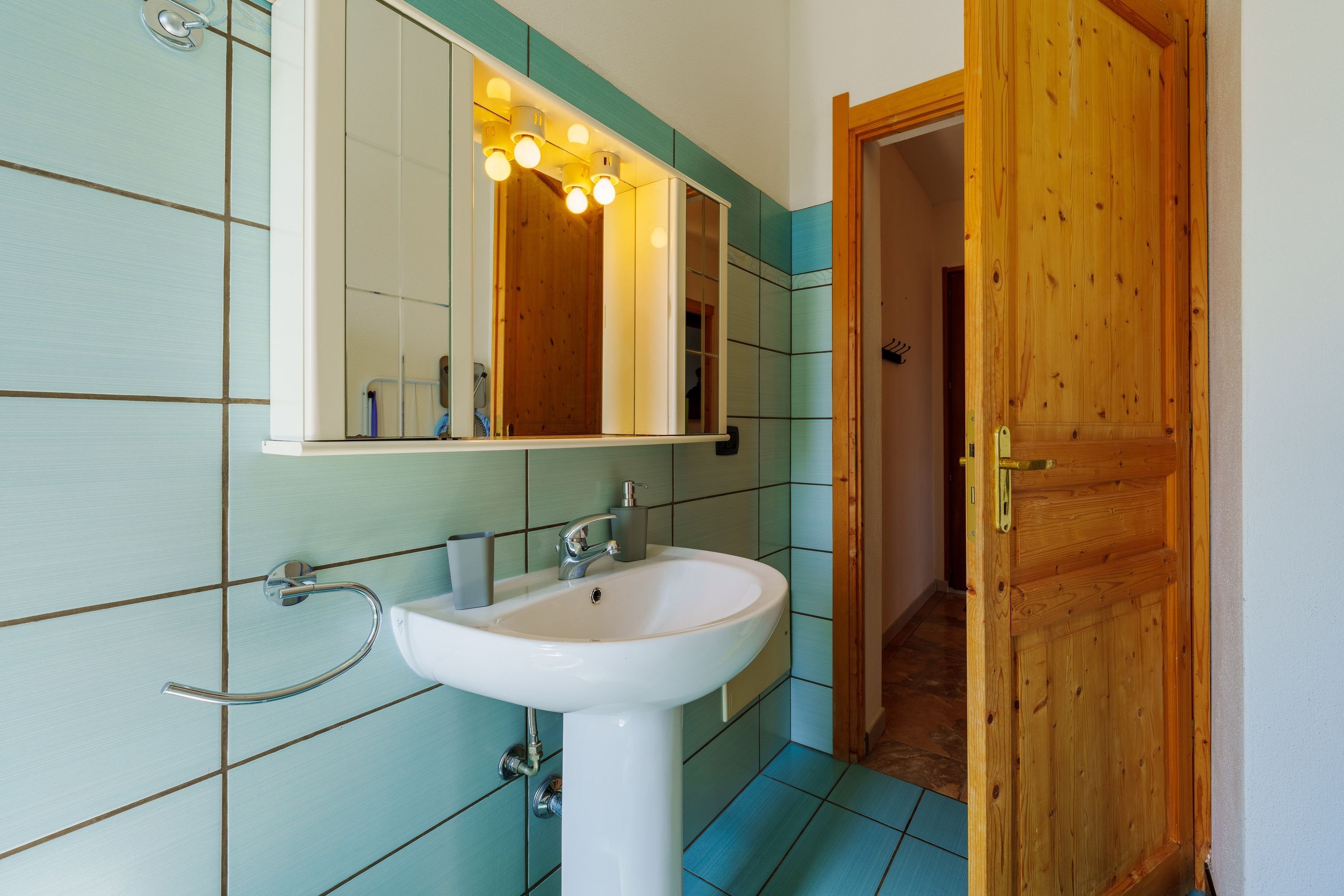 Un baño con un lavamanos blanco, un espejo y una puerta de madera.