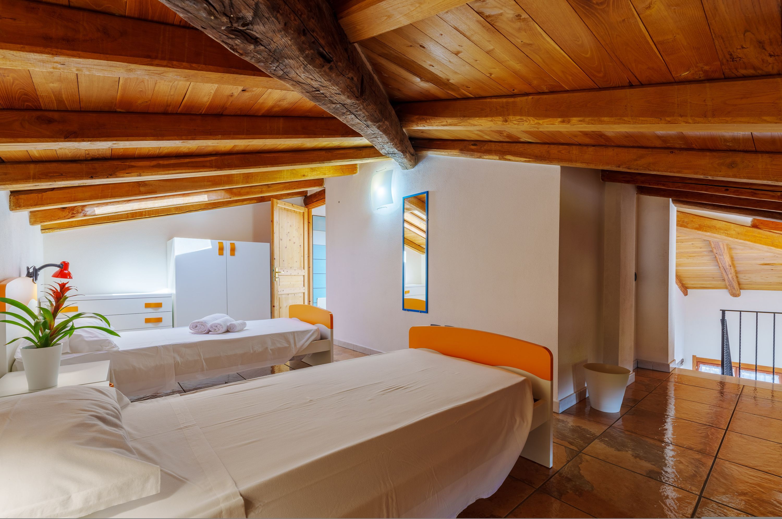 Ein Zimmer mit Holzbalken, einem Bett, einem Tisch, einem Stuhl, einer Topfpflanze und Blick auf einen Balkon.