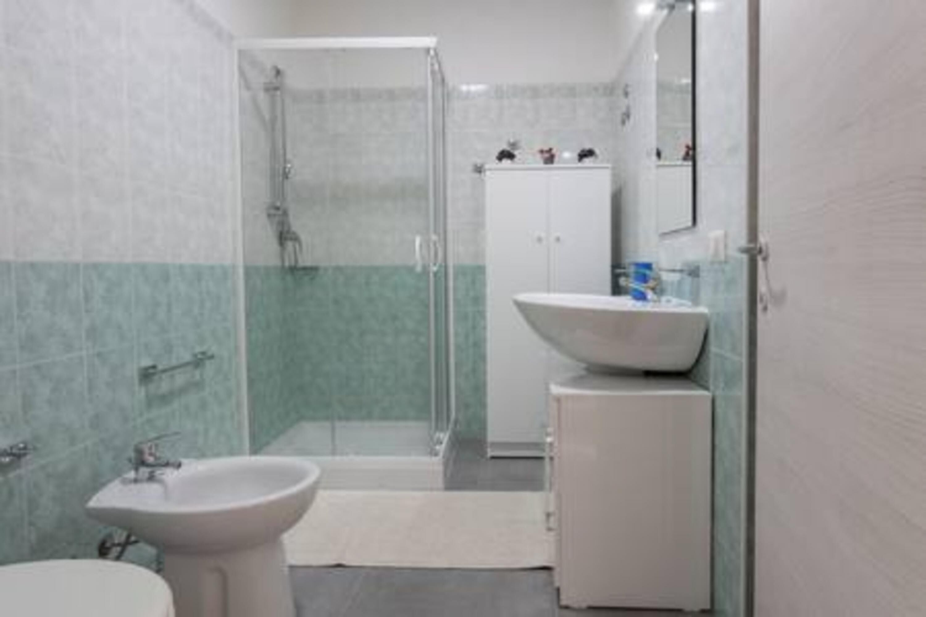 Un baño con cabina de ducha de vidrio, lavamanos pedestal y un mueble.