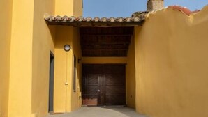 Une ruelle étroite, avec une porte en bois fermée au fond, bordée de murs jaunes.