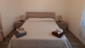 A single bed with a grey blanket, two bedside tables with lamps, and a stack of books on the left side. - Casa Aida al Centro di Nurachi (Nurachi)
